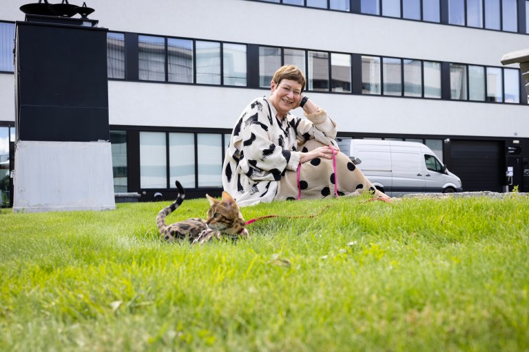 Portrett av Anne-Lise hammer med katten Oka på plenen utenfor et bygg ved FFI.